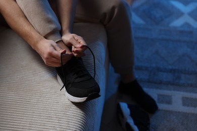 Photo of Man tying shoelace of sneaker at home, closeup