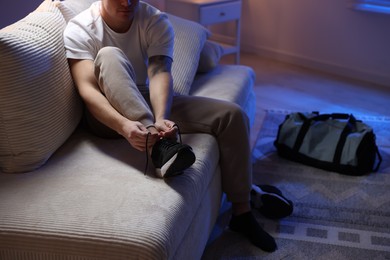 Photo of Man tying shoelace of sneaker at home, closeup