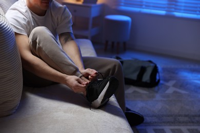 Photo of Man tying shoelace of sneaker at home, closeup