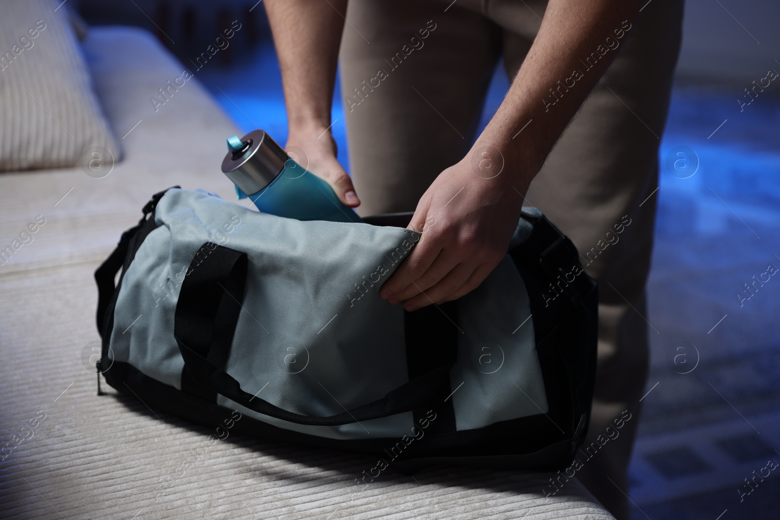 Photo of Man putting bottle of water into gym bag indoors, closeup