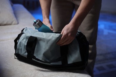 Photo of Man putting bottle of water into gym bag indoors, closeup