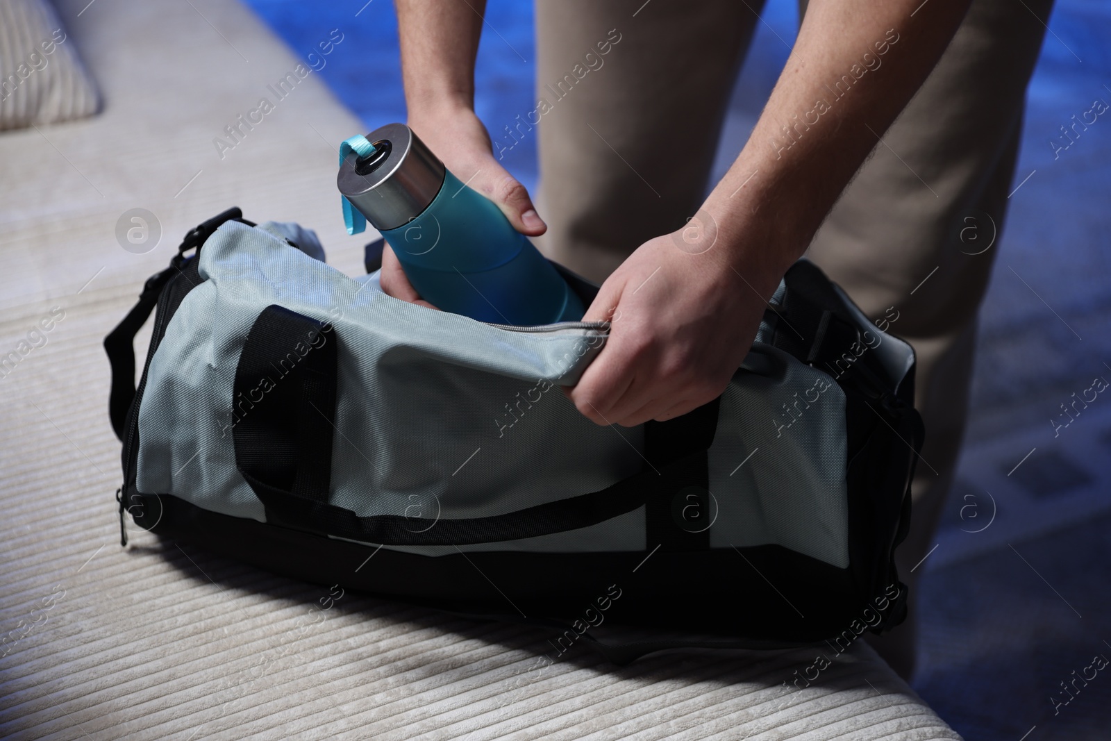 Photo of Man putting bottle of water into gym bag indoors, closeup