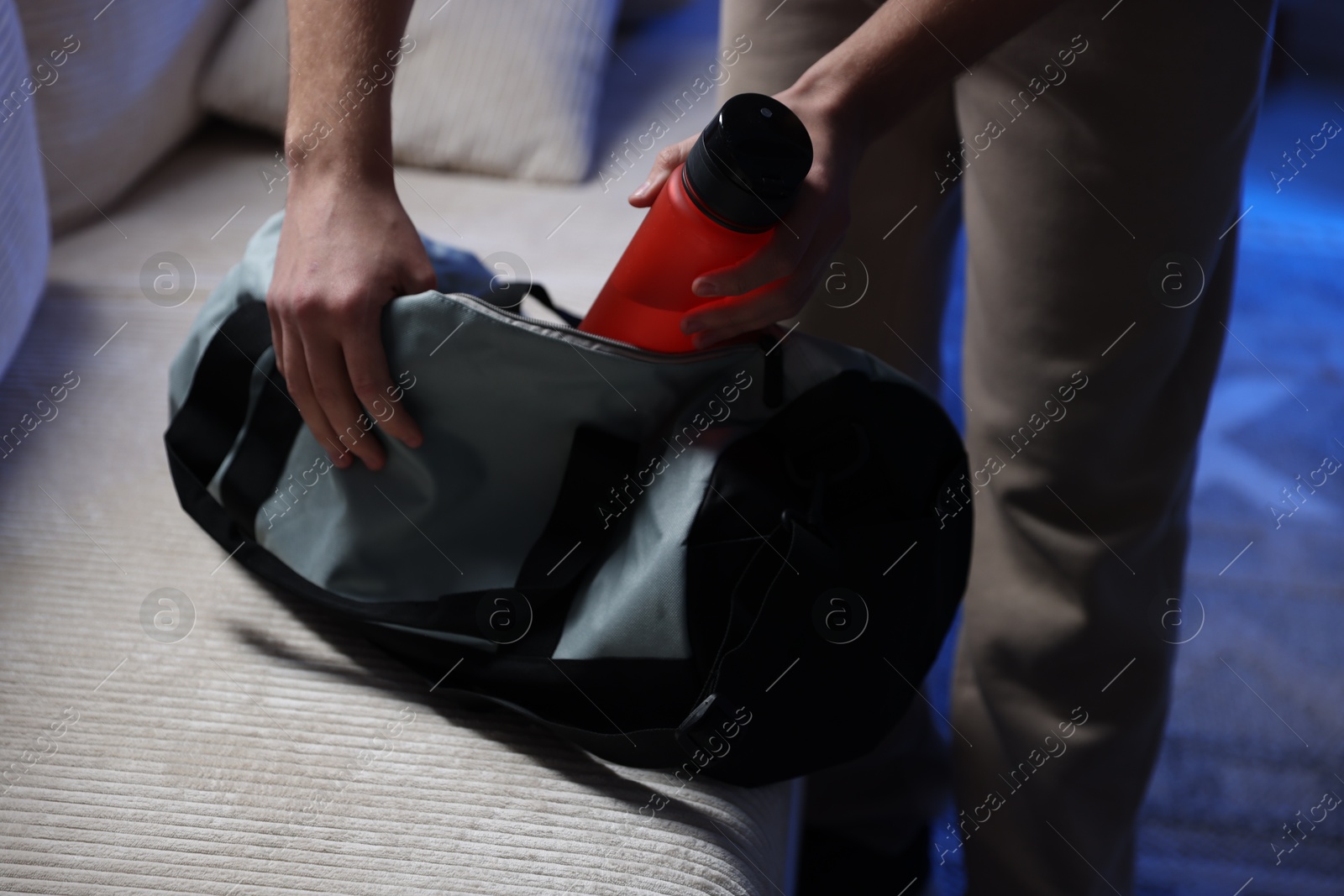 Photo of Man putting bottle of water into gym bag indoors, closeup