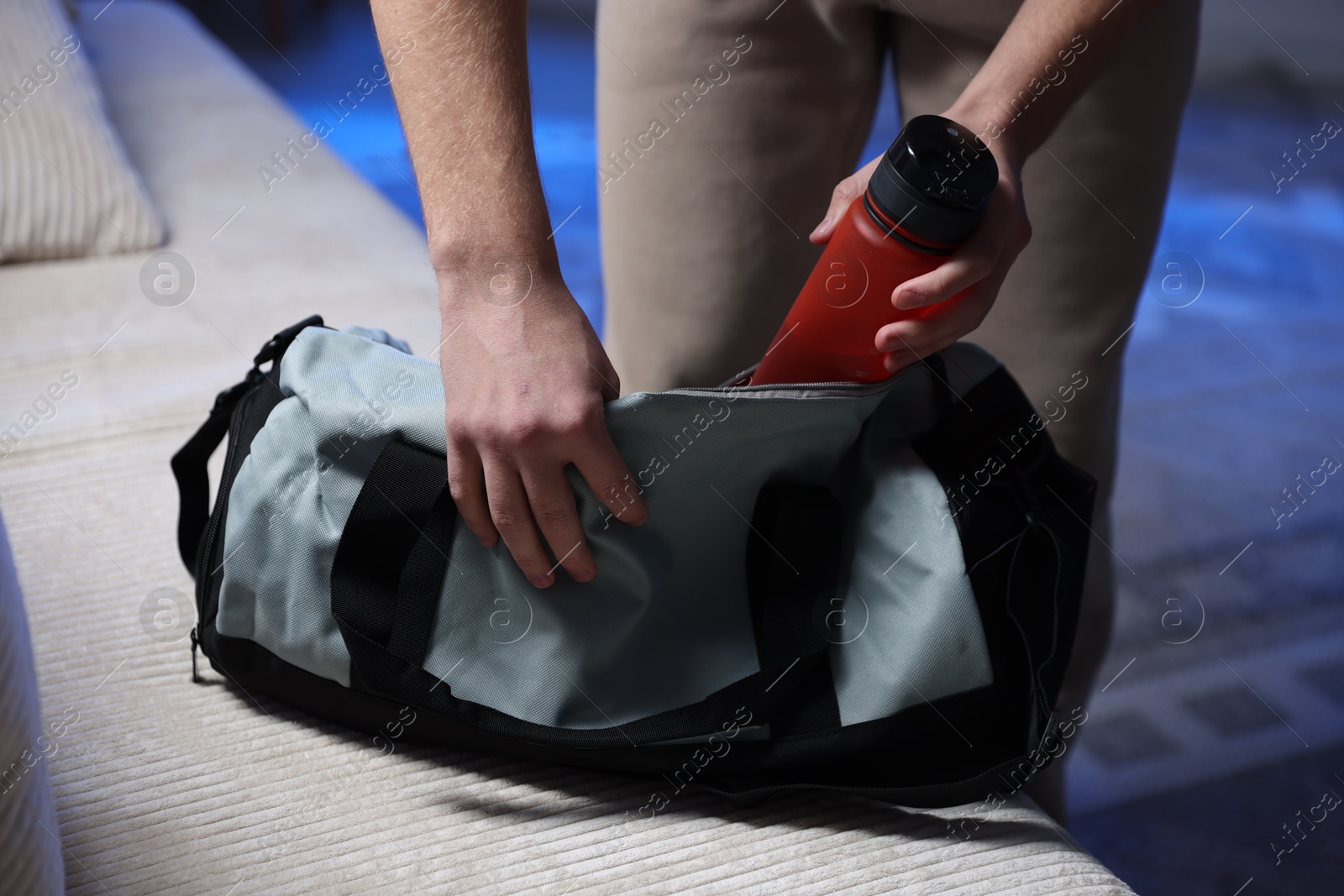 Photo of Man putting bottle of water into gym bag indoors, closeup