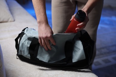 Photo of Man putting bottle of water into gym bag indoors, closeup