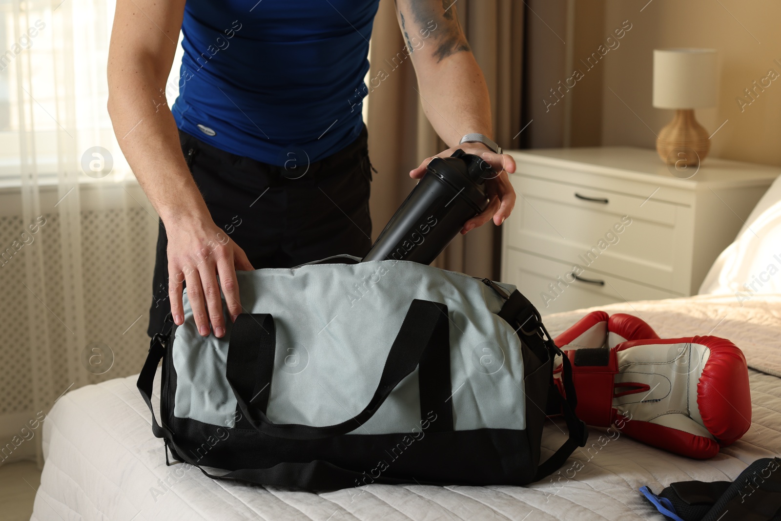 Photo of Man putting bottle of water into gym bag indoors, closeup