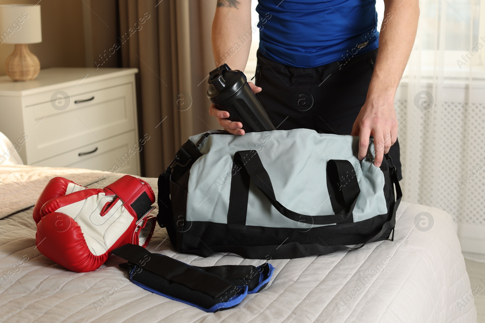 Photo of Man putting bottle of water into gym bag indoors, closeup