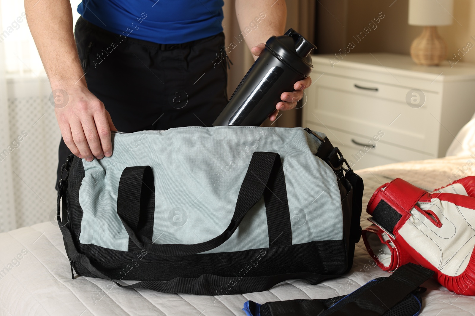 Photo of Man putting bottle of water into gym bag indoors, closeup