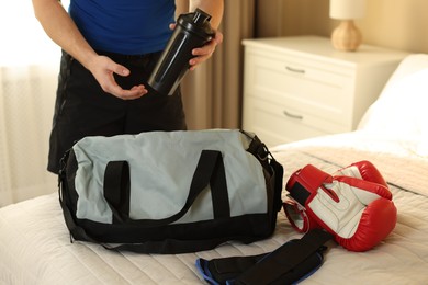 Photo of Man putting bottle of water into gym bag indoors, closeup