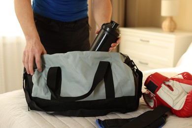 Photo of Man putting bottle of water into gym bag indoors, closeup