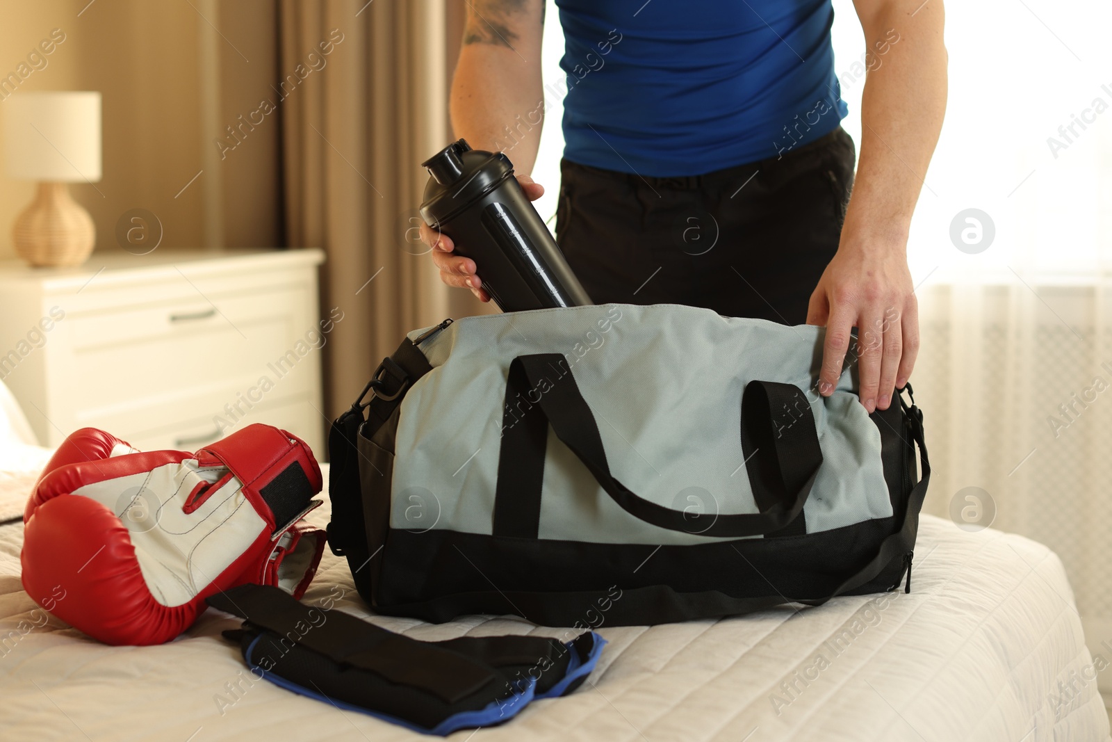 Photo of Man putting bottle of water into gym bag indoors, closeup