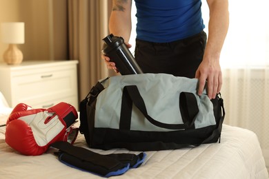 Photo of Man putting bottle of water into gym bag indoors, closeup