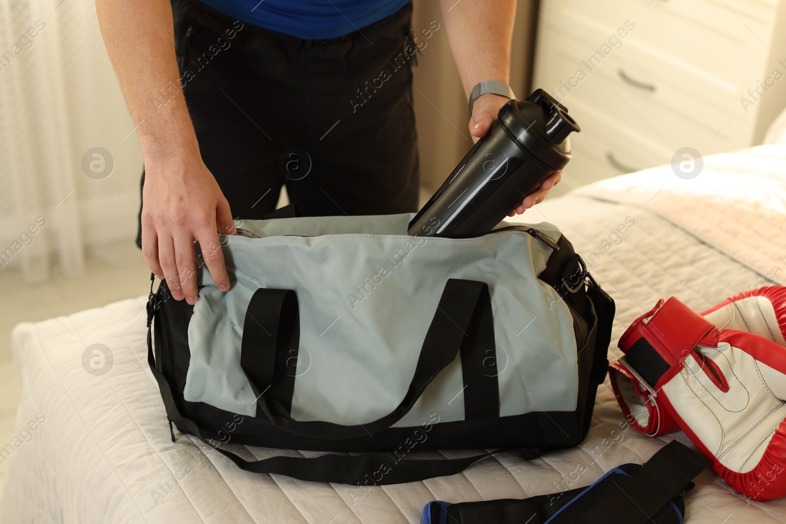 Photo of Man putting bottle of water into gym bag indoors, closeup