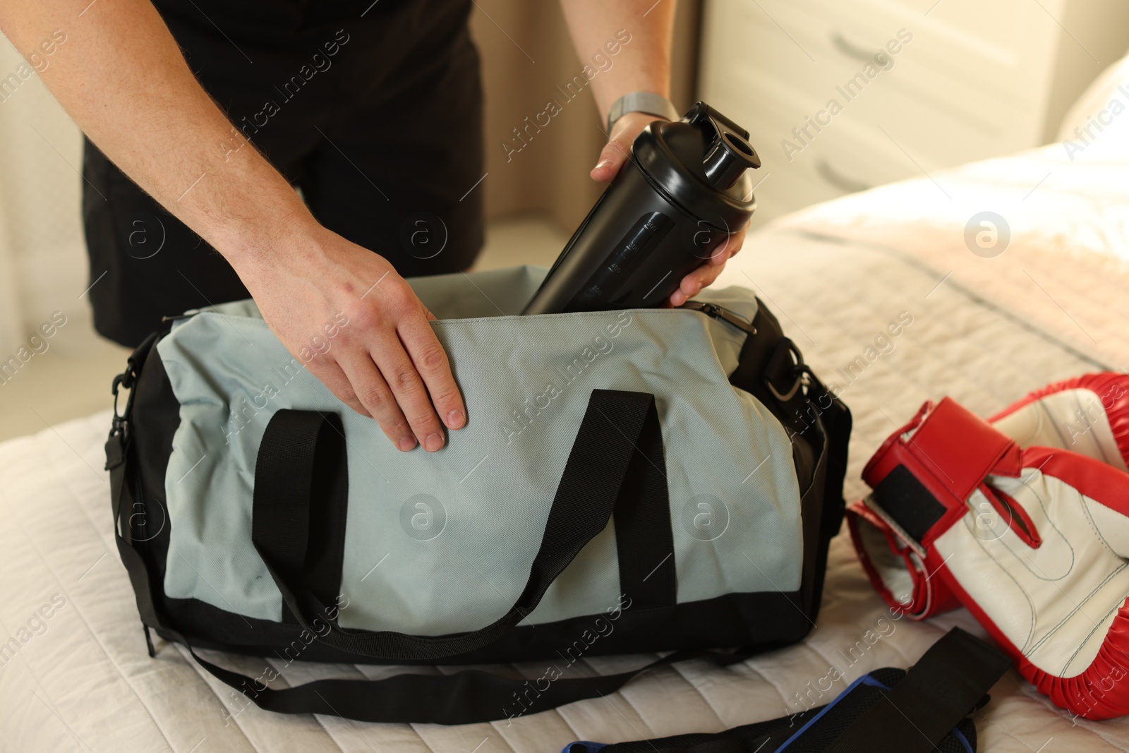 Photo of Man putting bottle of water into gym bag indoors, closeup