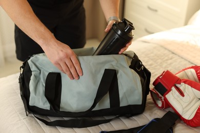 Photo of Man putting bottle of water into gym bag indoors, closeup