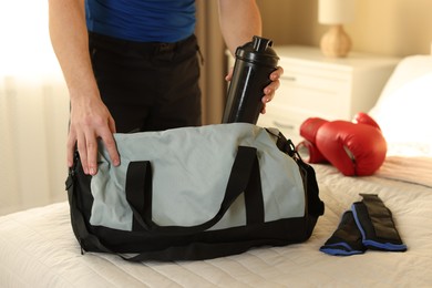 Photo of Man putting bottle of water into gym bag indoors, closeup