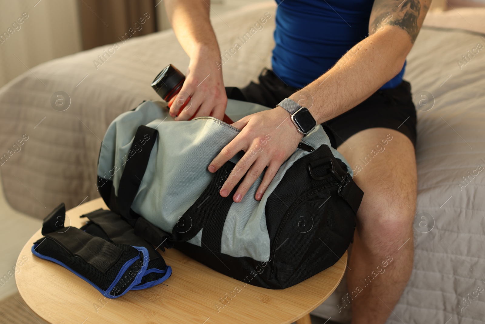 Photo of Man putting bottle of water into gym bag indoors, closeup