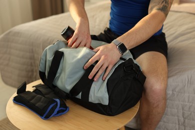 Photo of Man putting bottle of water into gym bag indoors, closeup