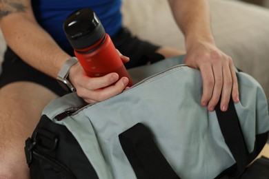 Photo of Man putting bottle of water into gym bag indoors, closeup