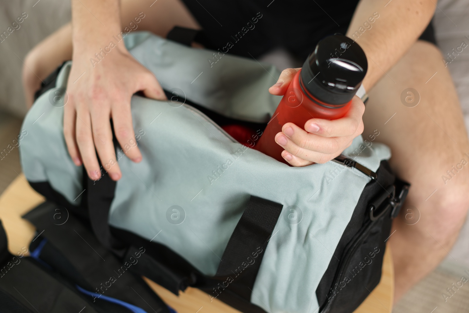 Photo of Man putting bottle of water into gym bag indoors, closeup