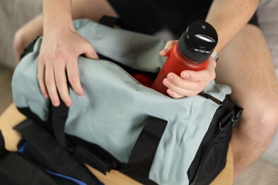 Photo of Man putting bottle of water into gym bag indoors, closeup