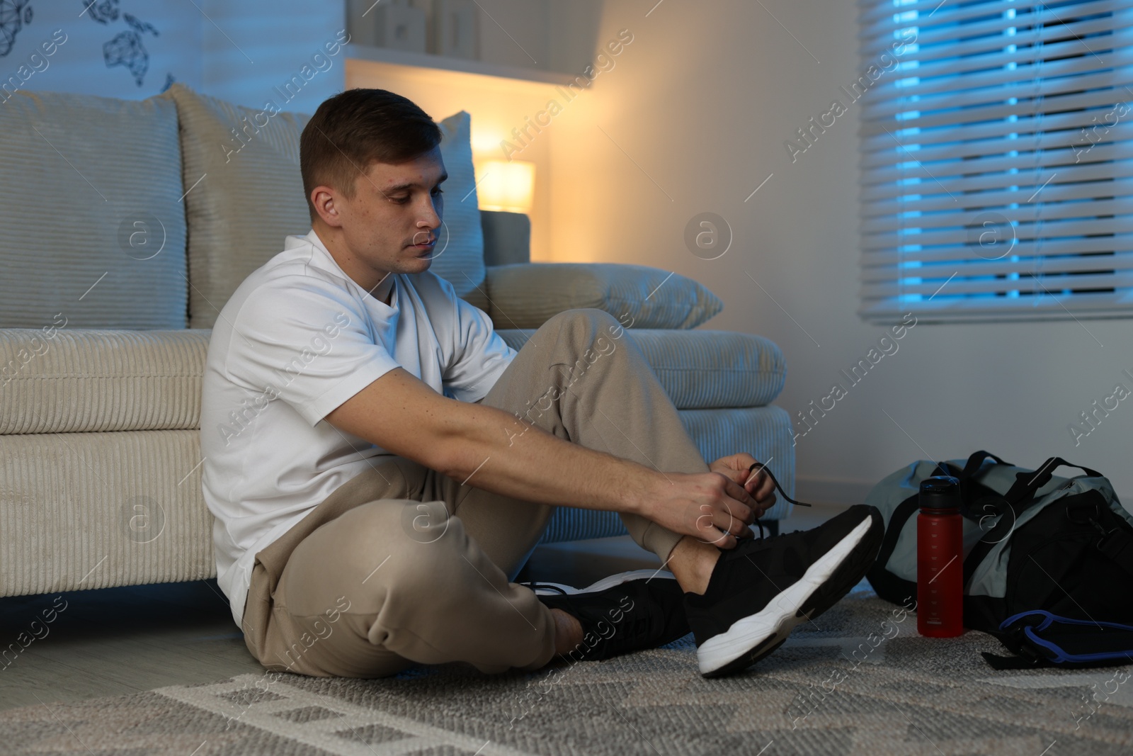 Photo of Young man tying shoelace of sneaker at home