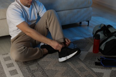 Photo of Man tying shoelace of sneaker at home, closeup