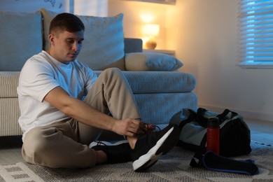 Photo of Young man tying shoelace of sneaker at home