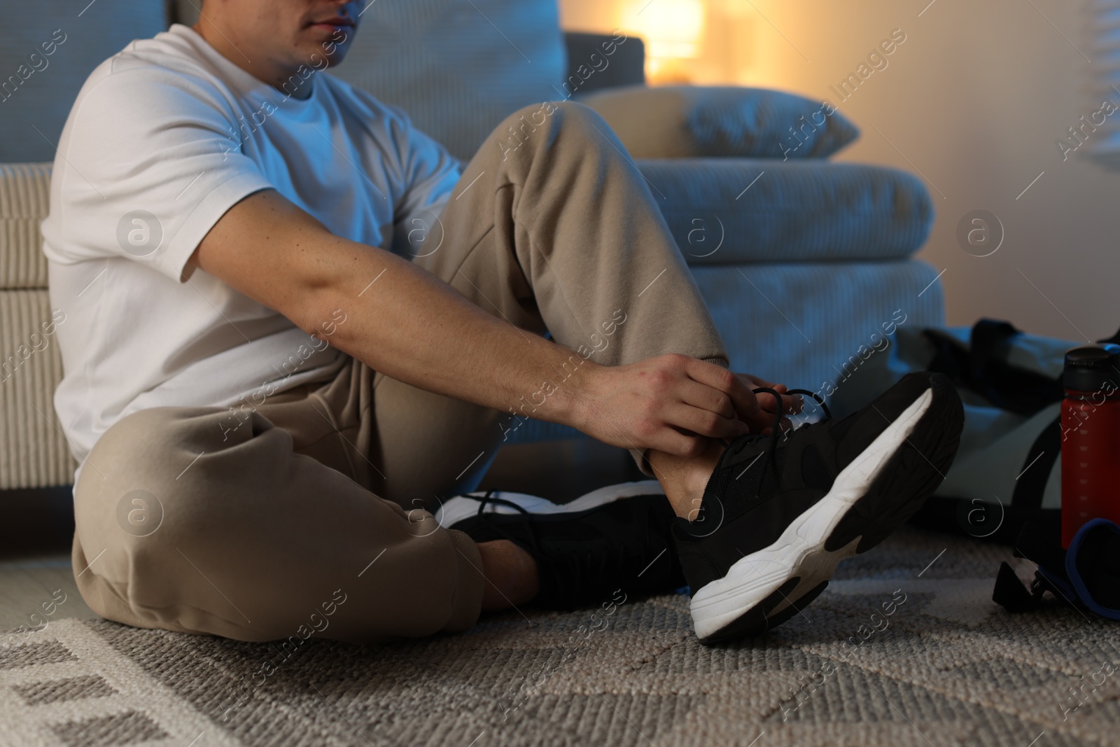 Photo of Man tying shoelace of sneaker at home, closeup