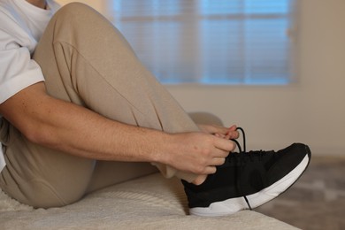 Photo of Man tying shoelace of sneaker at home, closeup