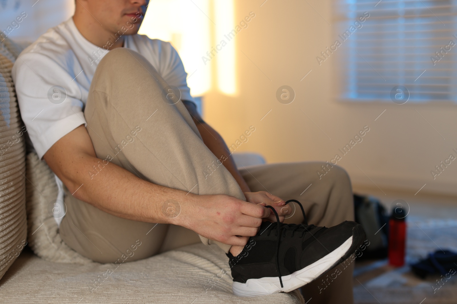 Photo of Man tying shoelace of sneaker at home, closeup