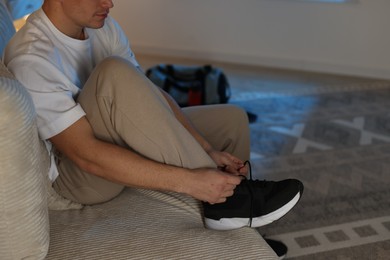 Photo of Man tying shoelace of sneaker at home, closeup