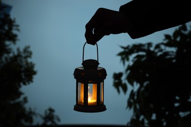 Photo of Woman holding Christmas lantern with burning candle in evening, closeup