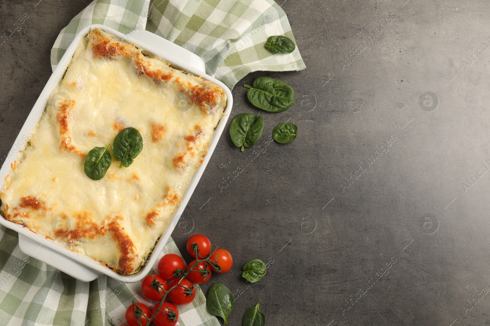 Photo of Delicious spinach lasagna in baking dish and ingredients on grey table, flat lay. Space for text