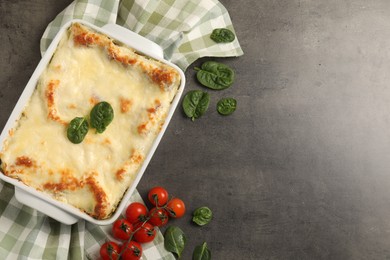 Photo of Delicious spinach lasagna in baking dish and ingredients on grey table, flat lay. Space for text