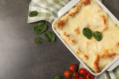 Photo of Delicious spinach lasagna in baking dish and ingredients on grey table, flat lay. Space for text