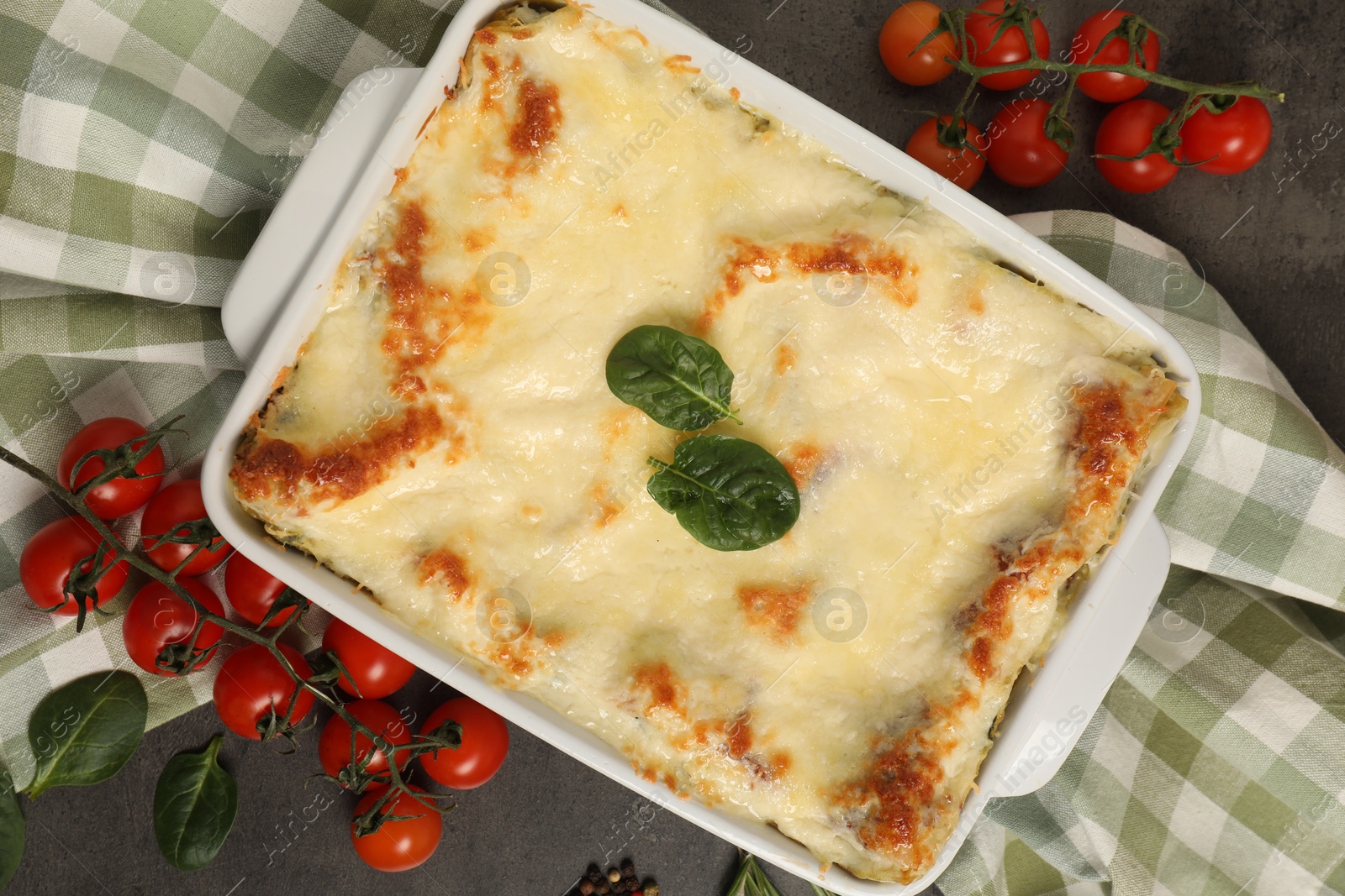 Photo of Delicious spinach lasagna in baking dish and ingredients on grey table, flat lay