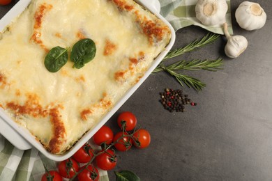 Photo of Delicious spinach lasagna in baking dish and ingredients on grey table, flat lay. Space for text