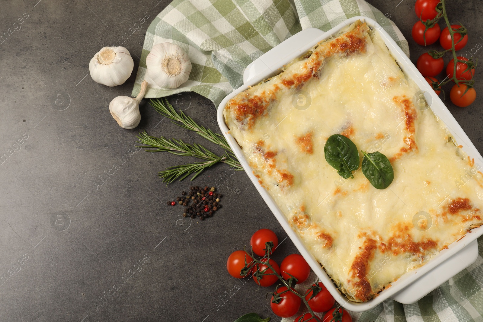 Photo of Delicious spinach lasagna in baking dish and ingredients on grey table, flat lay. Space for text