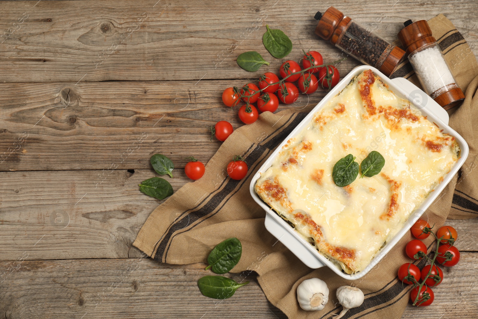 Photo of Delicious spinach lasagna in baking dish and ingredients on wooden table, flat lay. Space for text