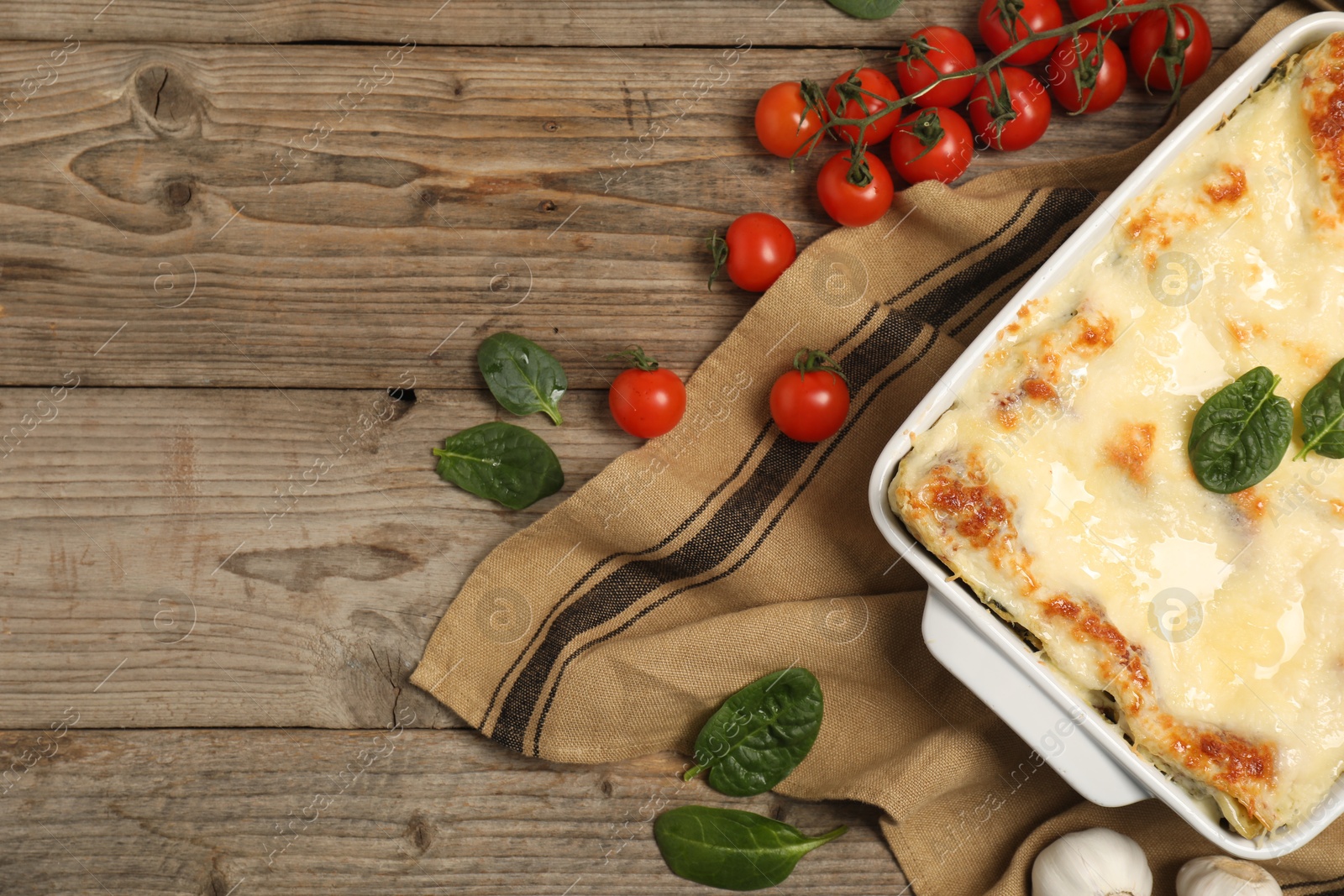 Photo of Delicious spinach lasagna in baking dish and ingredients on wooden table, flat lay. Space for text