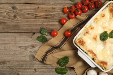 Photo of Delicious spinach lasagna in baking dish and ingredients on wooden table, flat lay. Space for text