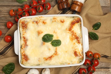 Photo of Delicious spinach lasagna in baking dish and ingredients on wooden table, flat lay