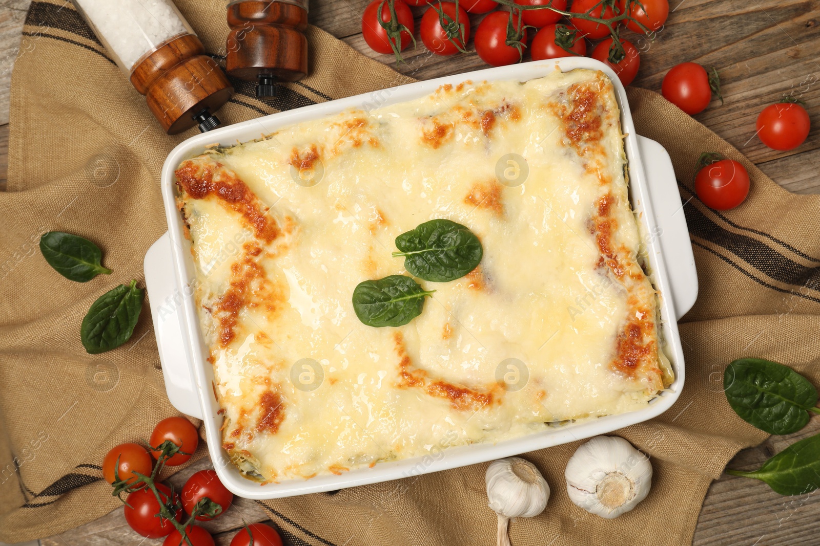 Photo of Delicious spinach lasagna in baking dish and ingredients on wooden table, flat lay