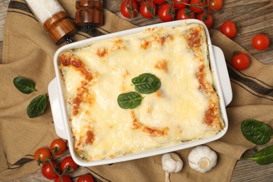 Photo of Delicious spinach lasagna in baking dish and ingredients on wooden table, flat lay