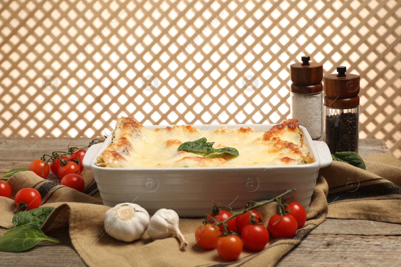 Photo of Delicious spinach lasagna in baking dish and ingredients on wooden table