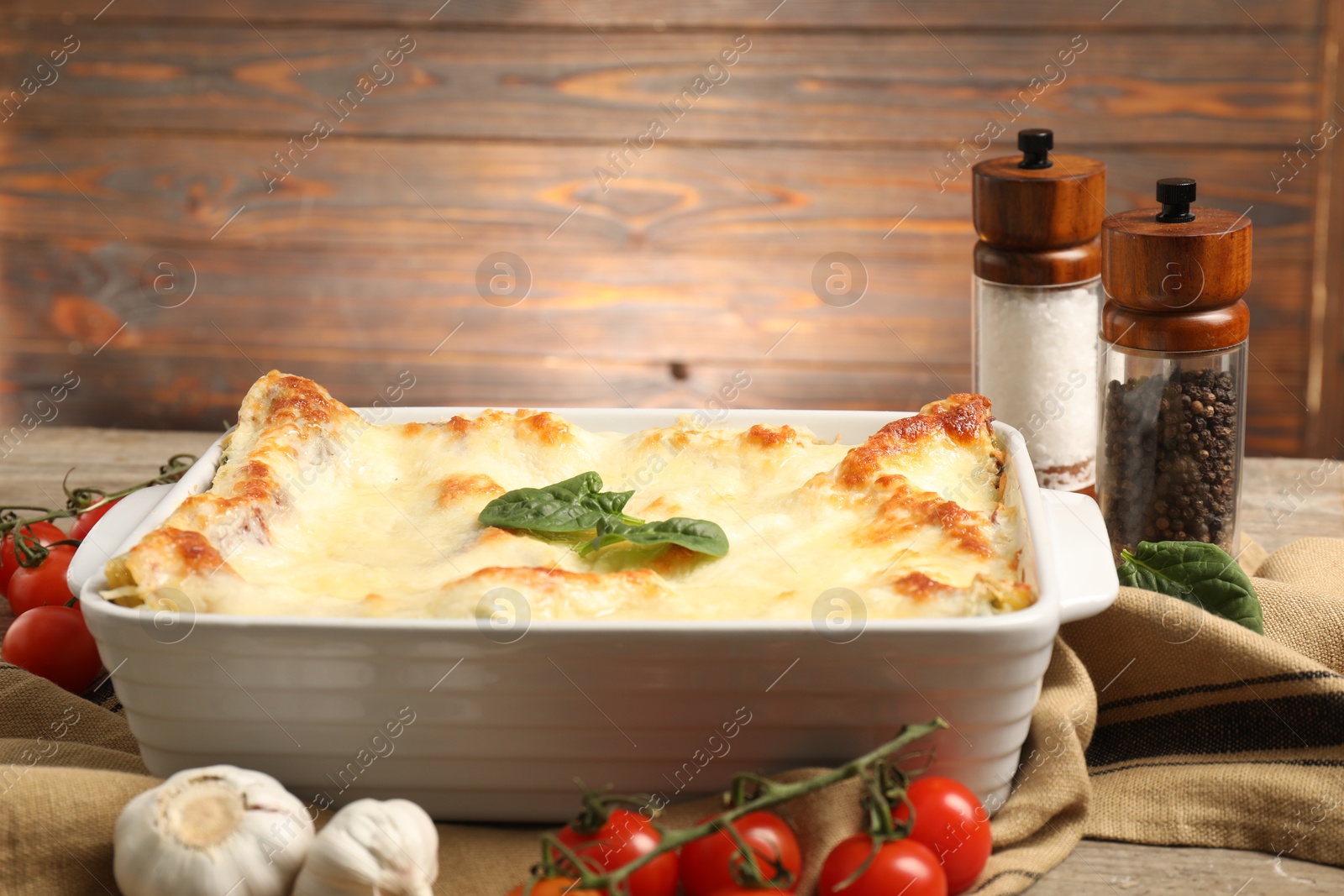 Photo of Delicious spinach lasagna in baking dish and ingredients on wooden table