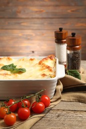 Photo of Delicious spinach lasagna in baking dish and ingredients on wooden table