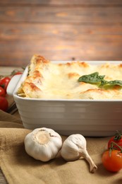 Photo of Delicious spinach lasagna in baking dish and ingredients on table, closeup