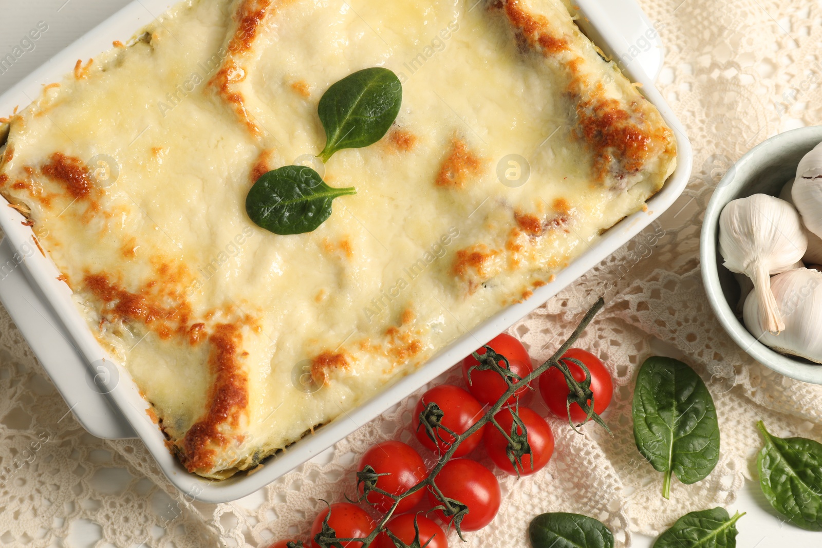 Photo of Delicious spinach lasagna in baking dish and ingredients on white table, flat lay